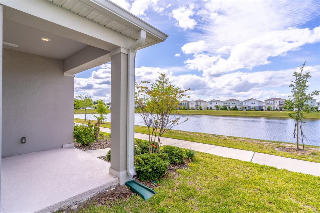 A covered patio overlooks a pond and a sidewalk with houses in the background — 6074 WINDY LEAF ALLEY, ST CLOUD, FL