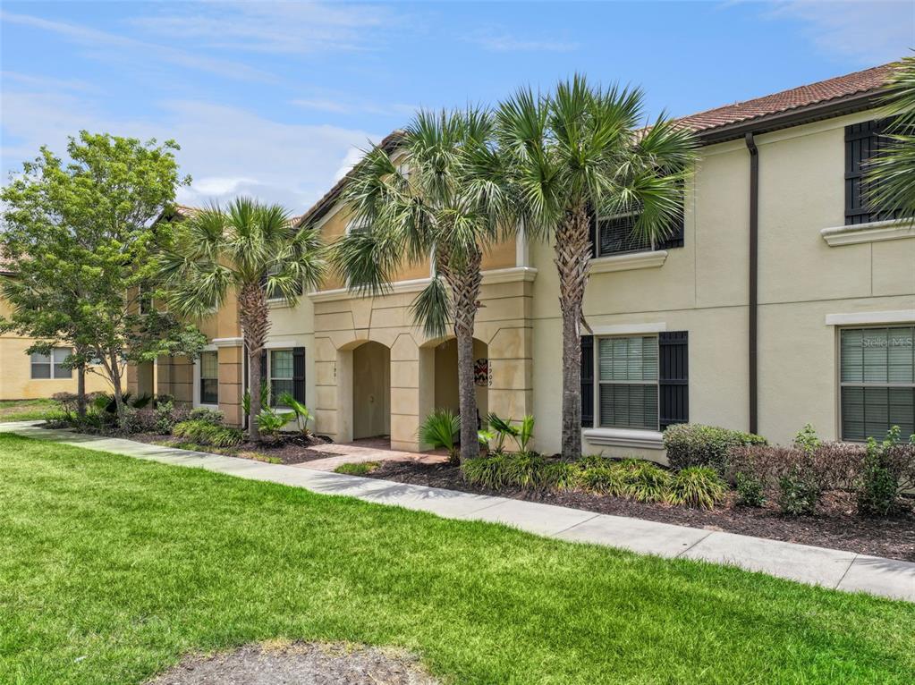 A two-story tan stucco building features arched entryways, palm trees, and a front sidewalk — 1909 MAJORCA DRIVE, KISSIMMEE, FL