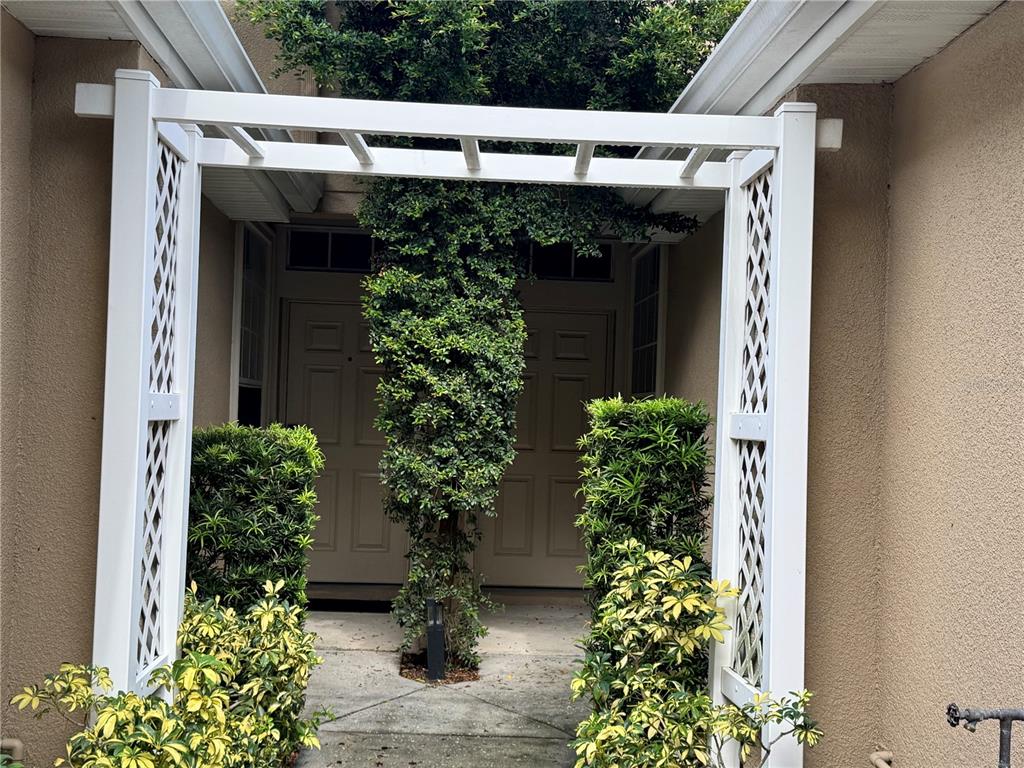 A white trellis stands over a walkway leading to a front door with surrounding landscaping — 4107 KEY THATCH DRIVE, TAMPA, FL
