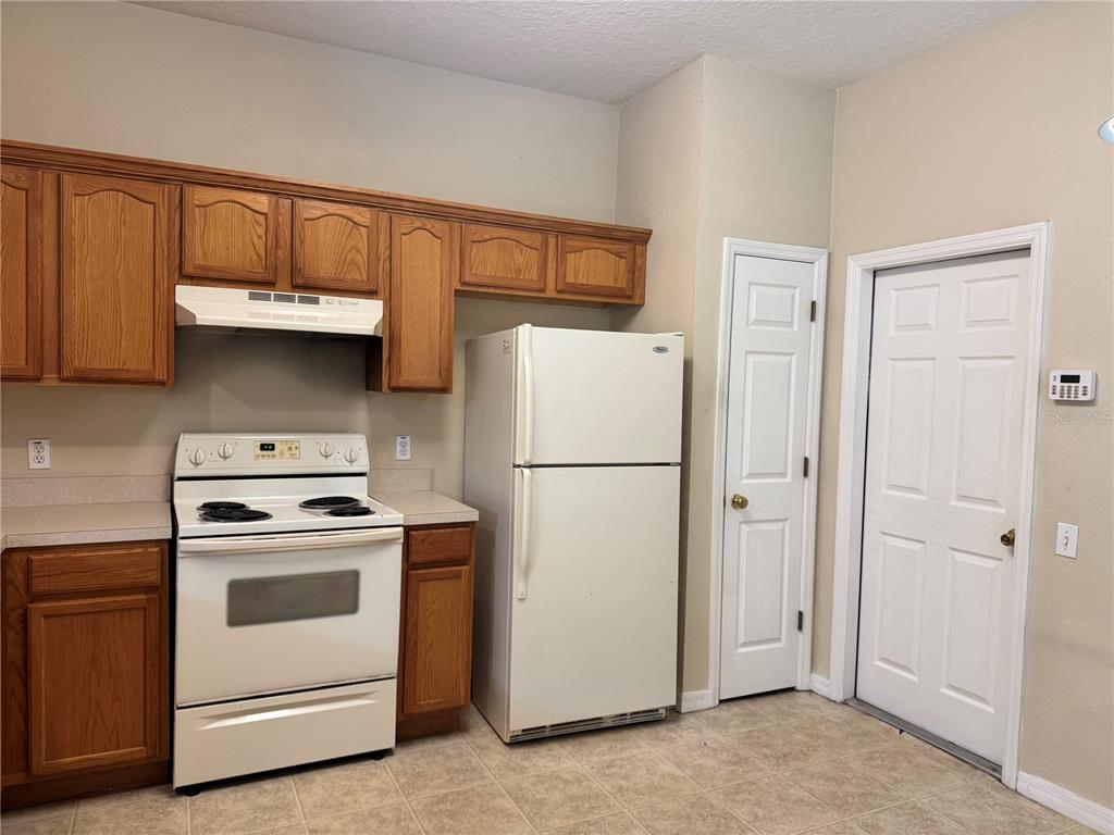 A kitchen features oak cabinets, white appliances, a tiled floor, and two white doors — 4107 KEY THATCH DRIVE, TAMPA, FL