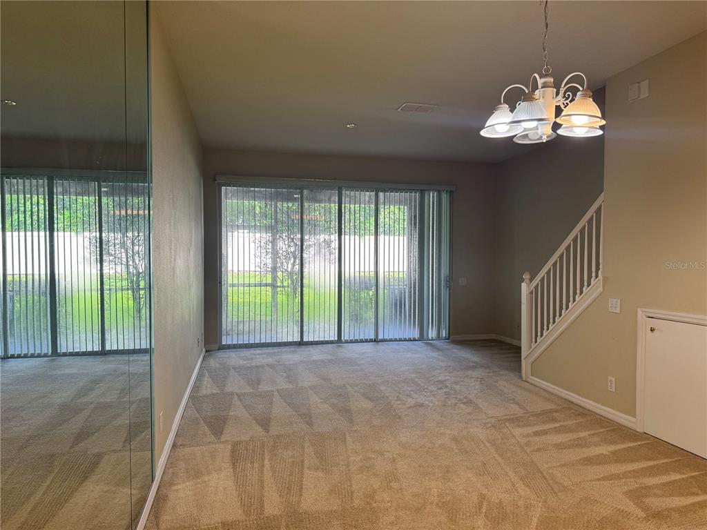 A carpeted living room features a mirrored wall, a chandelier, and sliding glass patio doors — 4107 KEY THATCH DRIVE, TAMPA, FL