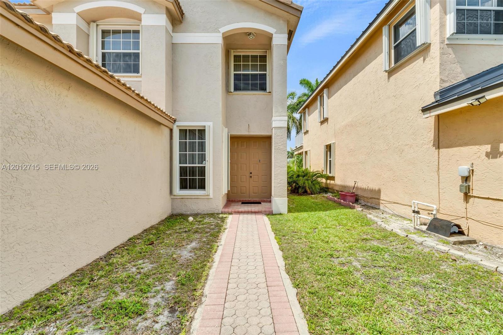 A paved walkway leads to the front entrance of a two-story stucco house — 18081 SW 33rd St, Miramar FL 33029, MIRAMAR, FL
