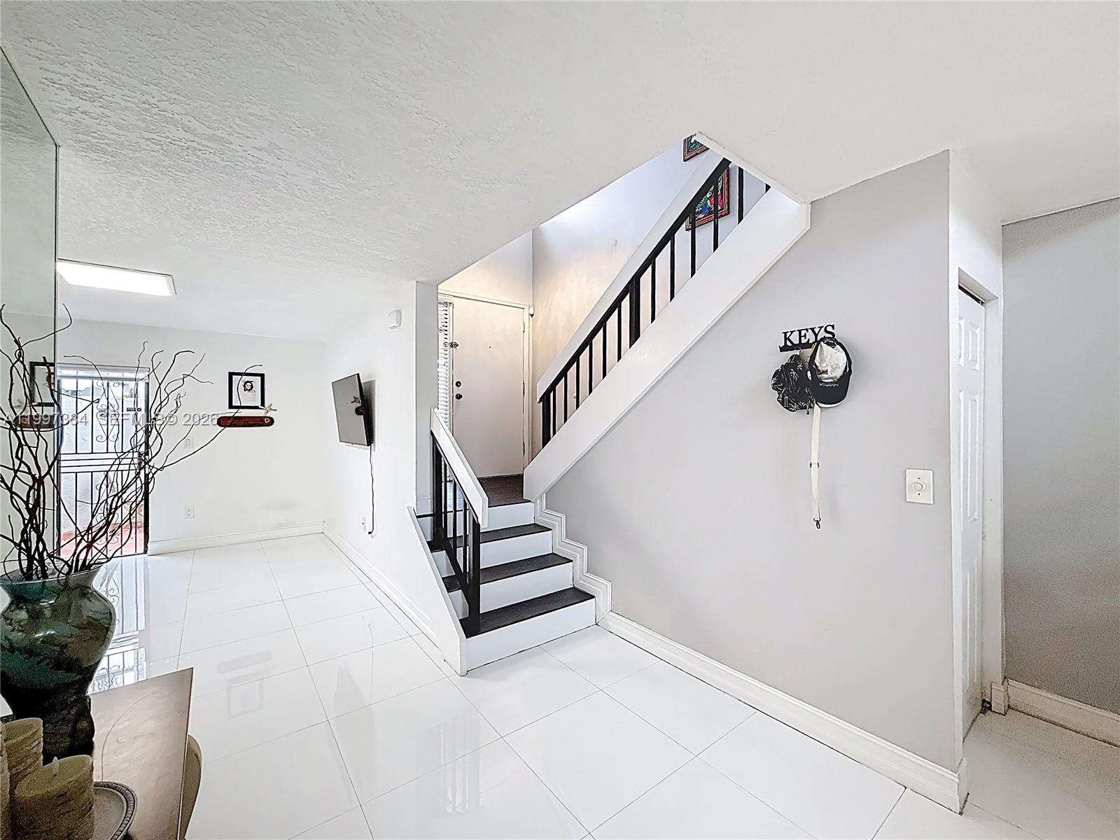 An entryway features white tile floors, a staircase with black treads, and a key rack — 1291 SW 124th Ct # B, Miami FL 33184, MIAMI, FL