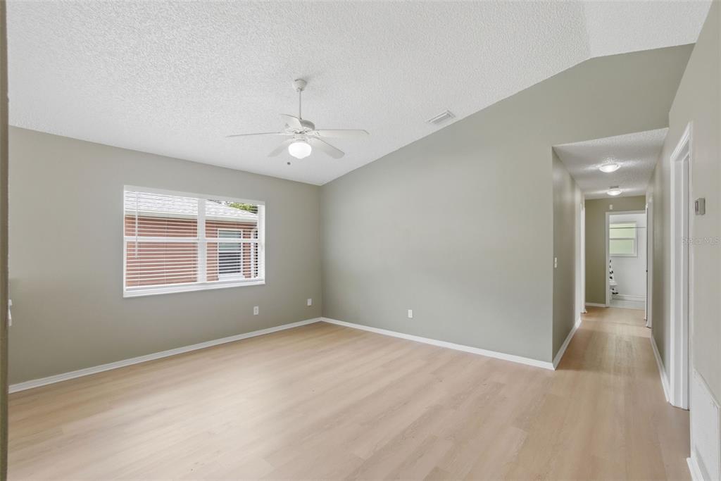 An empty bedroom with light wood-look flooring, gray walls, a ceiling fan, and a hallway — 2308 DONEGAN PLACE, ORLANDO, FL