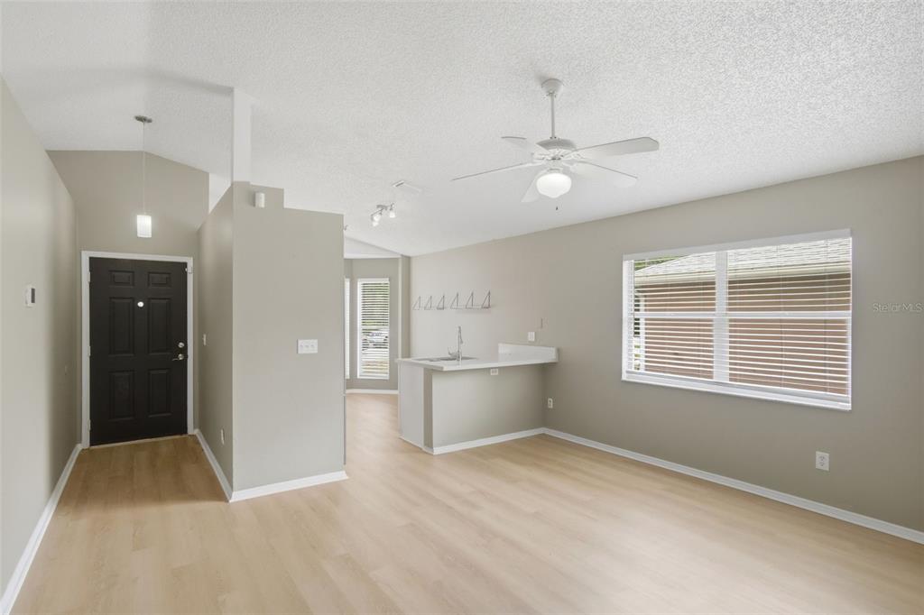 A living room with light wood-look flooring, a ceiling fan, and an open kitchen counter — 2308 DONEGAN PLACE, ORLANDO, FL