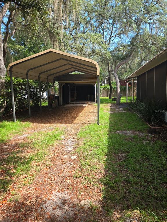 A metal carport stands in a grassy yard next to a house with a screened porch — 18927 SE 18TH PLACE, SILVER SPRINGS, FL
