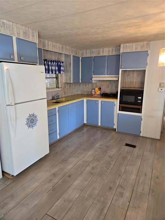 A kitchen features blue cabinets, a white refrigerator, wood-look flooring, and a built-in microwave — 18927 SE 18TH PLACE, SILVER SPRINGS, FL