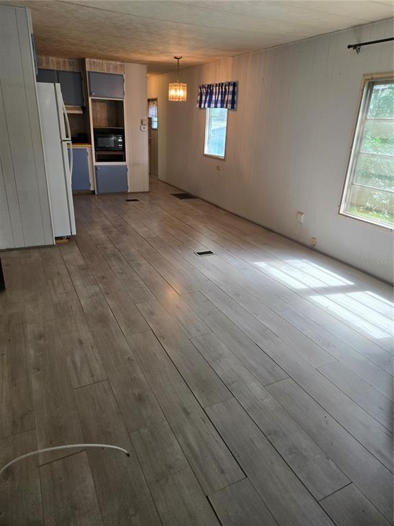 A long, open-concept room features light wood-look flooring, white paneled walls, and a kitchen area — 18927 SE 18TH PLACE, SILVER SPRINGS, FL