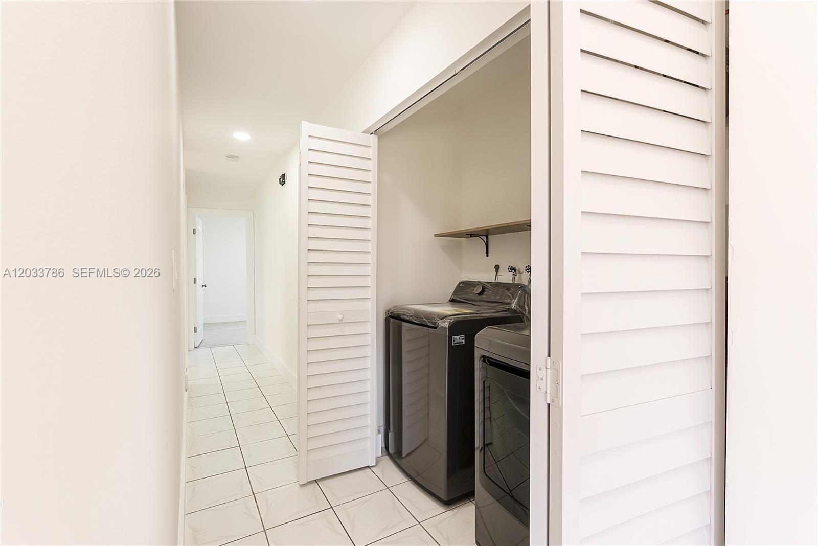 A laundry closet with dark appliances and a shelf is located in a tiled hallway — 15881 SW 139th Ave, Miami FL 33177, MIAMI, FL