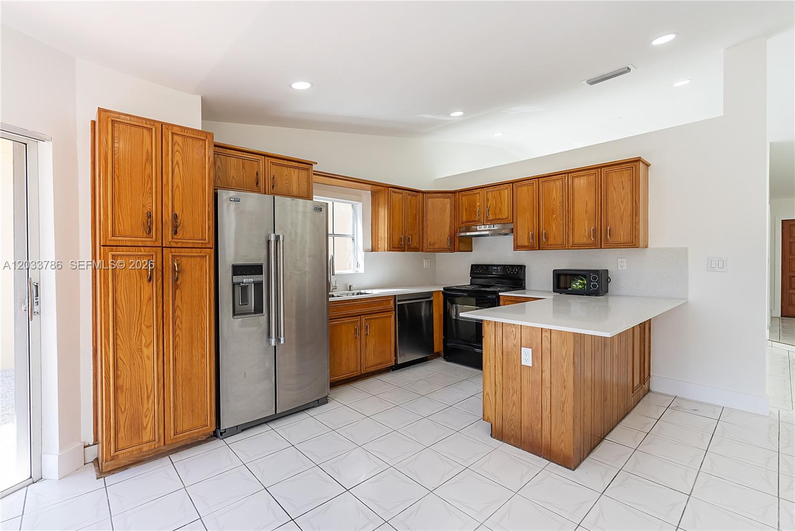 A kitchen features oak cabinets, stainless steel appliances, white countertops, and white tile flooring — 15881 SW 139th Ave, Miami FL 33177, MIAMI, FL