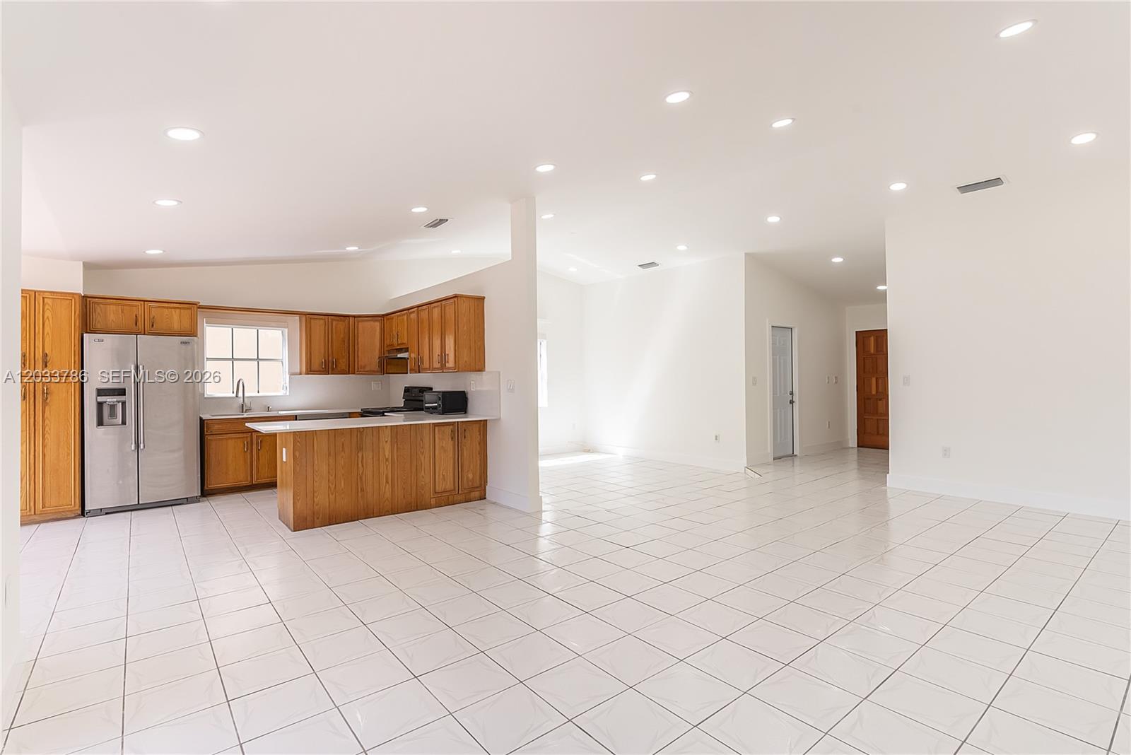A kitchen with wood cabinets and stainless steel appliances opens into a large tiled room — 15881 SW 139th Ave, Miami FL 33177, MIAMI, FL