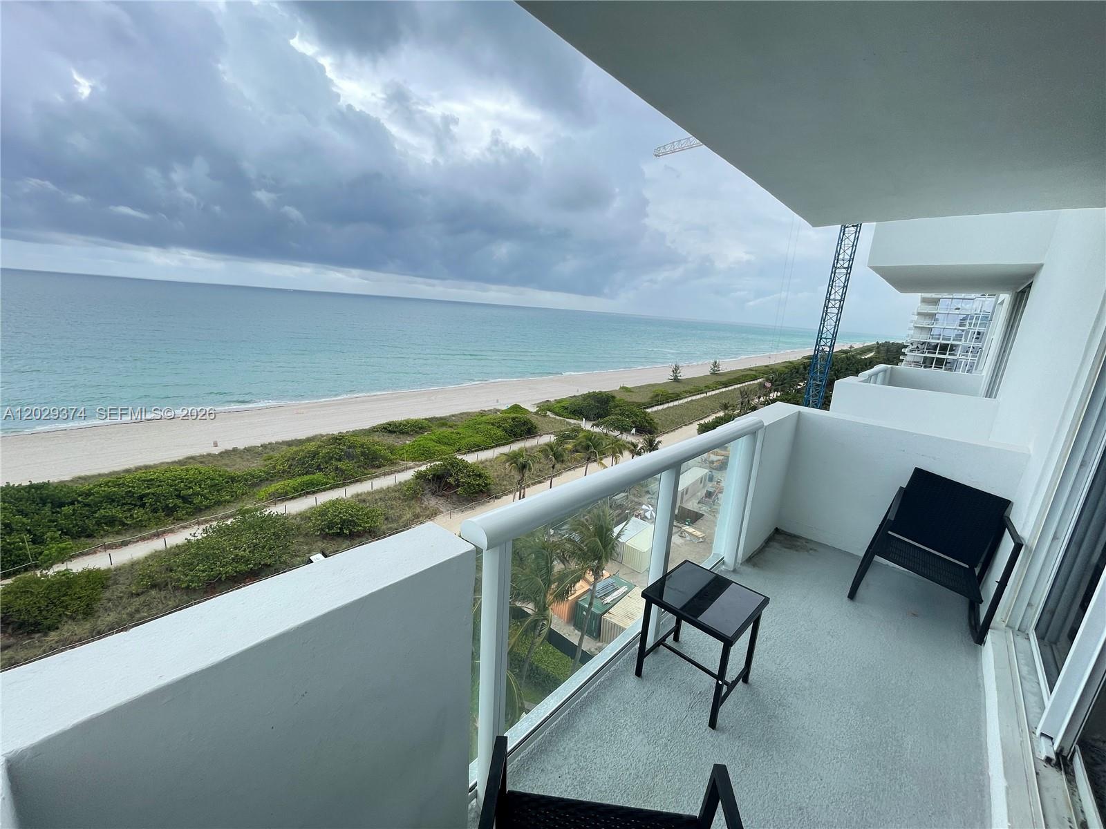 A balcony with a glass railing overlooks a sandy beach and the ocean — 9195 Collins Ave # 1001, Surfside FL 33154, SURFSIDE, FL