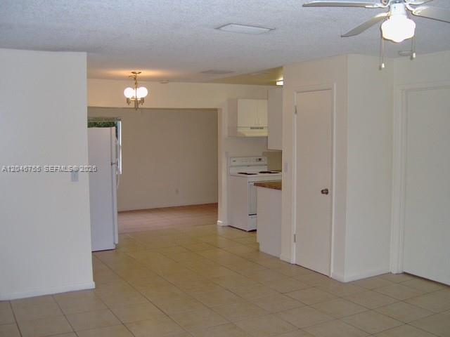 An interior view shows a tiled living area leading to a kitchen with white appliances — PALM BEACH GARDENS, FL