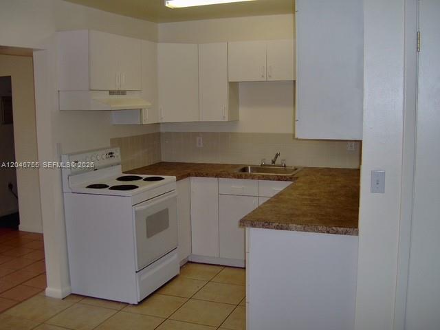 A kitchen features white cabinets, a white stove, and brown countertops over tiled floors — PALM BEACH GARDENS, FL