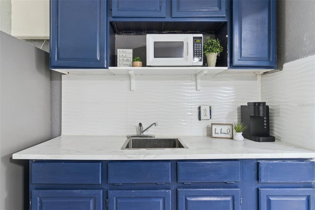 A kitchen kitchenette features blue cabinets, a white marble countertop, a sink, and a microwave — 43420 HIGHWAY 27 UNIT 464, DAVENPORT, FL