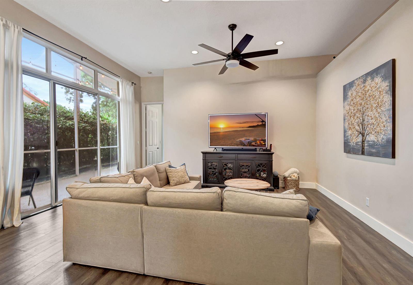 A living room features a sectional sofa, a television on a console, and sliding glass doors — 23437 Water Circle, Boca Raton FL 33486, BOCA RATON, FL