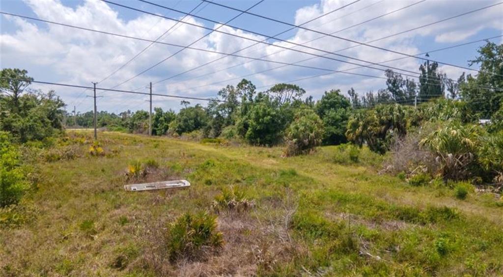 A grassy, undeveloped lot features scattered low vegetation and overhead power lines under a sky — 925 INDIAN CREEK LANE, PUNTA GORDA, FL