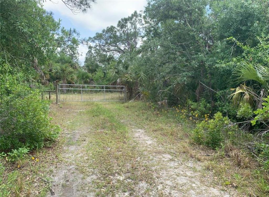 A metal gate blocks a dirt path leading into a wooded area with dense vegetation — 925 INDIAN CREEK LANE, PUNTA GORDA, FL