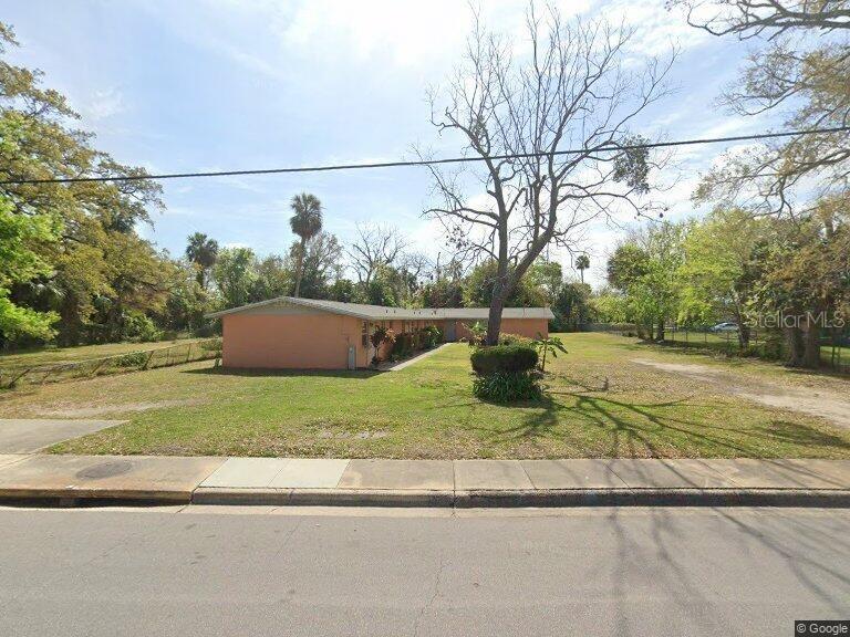 A single-story peach-colored apartment building sits on a grassy lot with several large trees — 555 OAK STREET, DAYTONA BEACH, FL