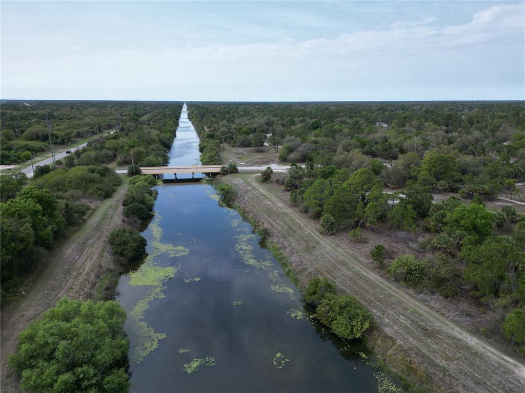 An aerial view shows a narrow canal flowing under a bridge through a wooded area — S RAINTREE BOULEVARD, NORTH PORT, FL