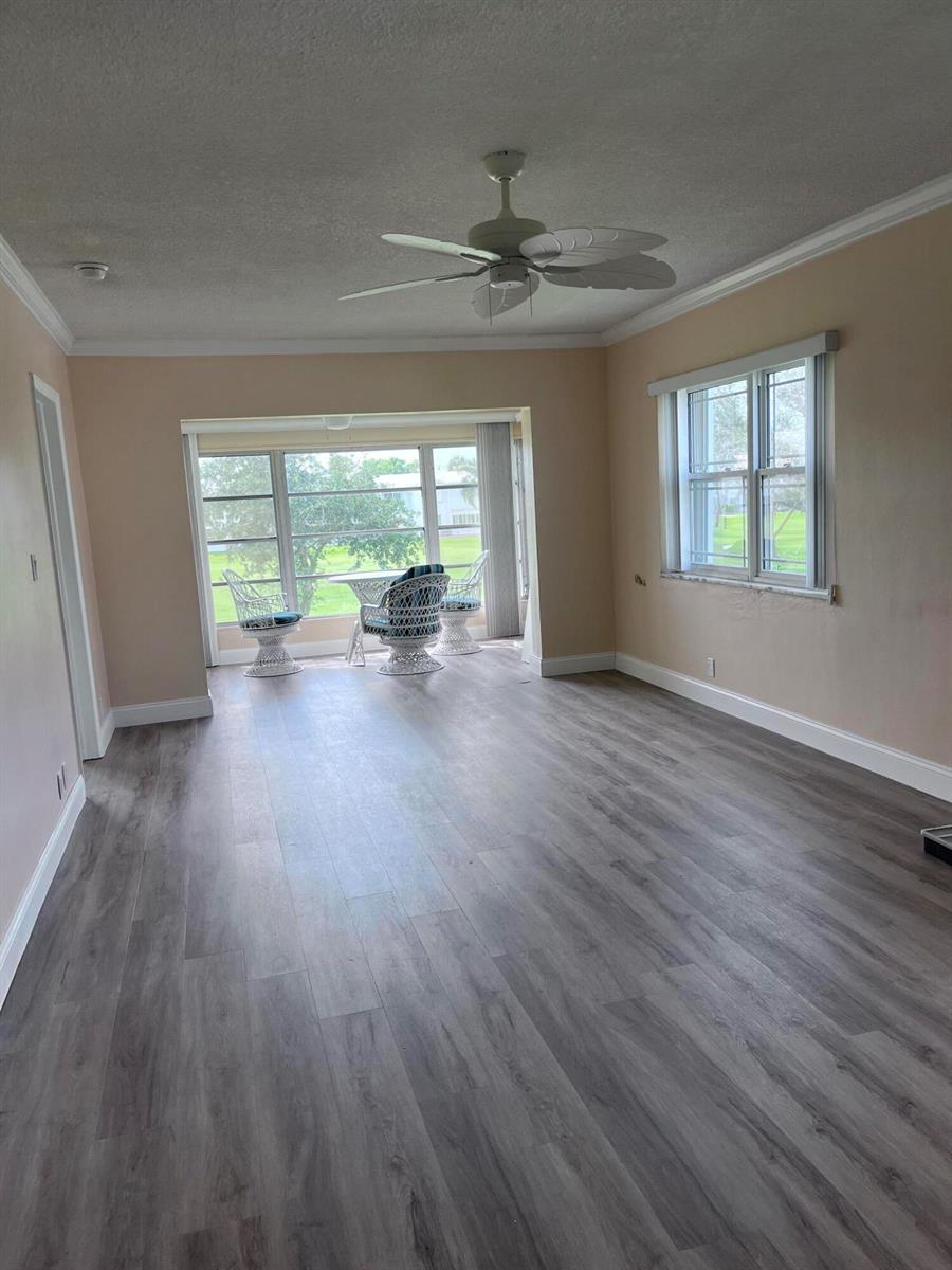 A living room with light-colored walls, gray wood-look flooring, a ceiling fan, and large windows — 251 S Golf # 294, Pompano Beach FL 33064, POMPANO BEACH, FL
