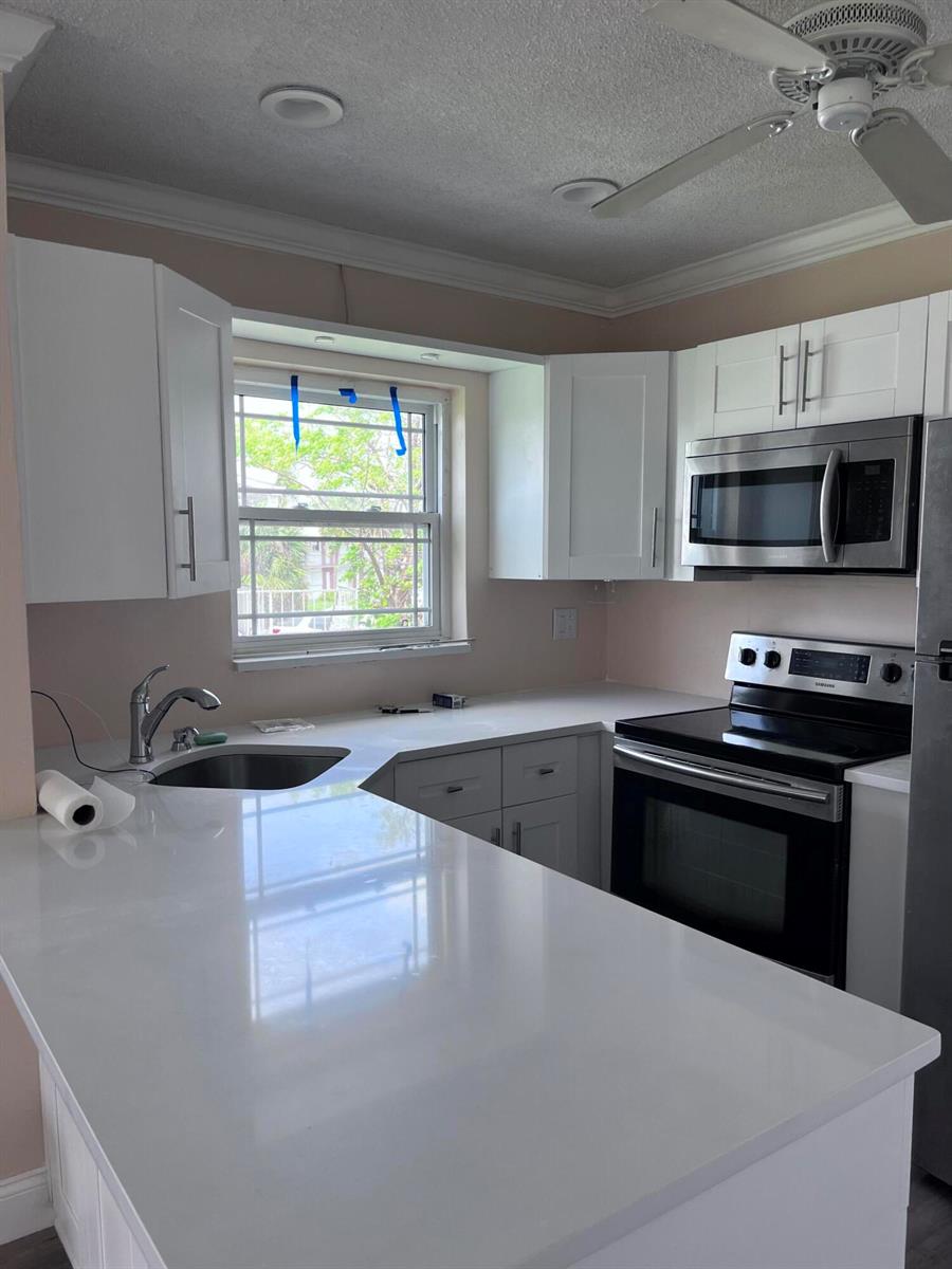 A kitchen features white cabinets, stainless steel appliances, and white countertops under a ceiling fan — 251 S Golf # 294, Pompano Beach FL 33064, POMPANO BEACH, FL