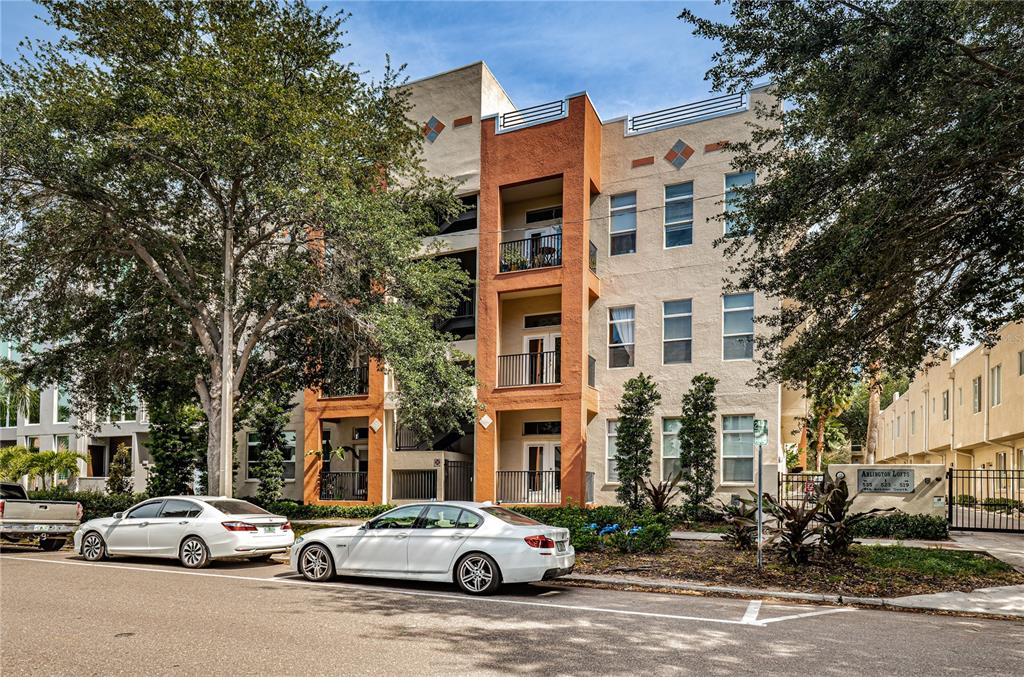 A multi-story apartment building with orange accents and balconies sits behind two parked white cars — 535 4TH AVENUE S UNIT 4, ST PETERSBURG, FL