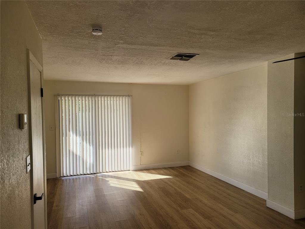 An empty room features light wood-look flooring, off-white walls, and vertical blinds over a sliding door — 1236 DOVEHILL DRIVE UNIT 1244, APOPKA, FL