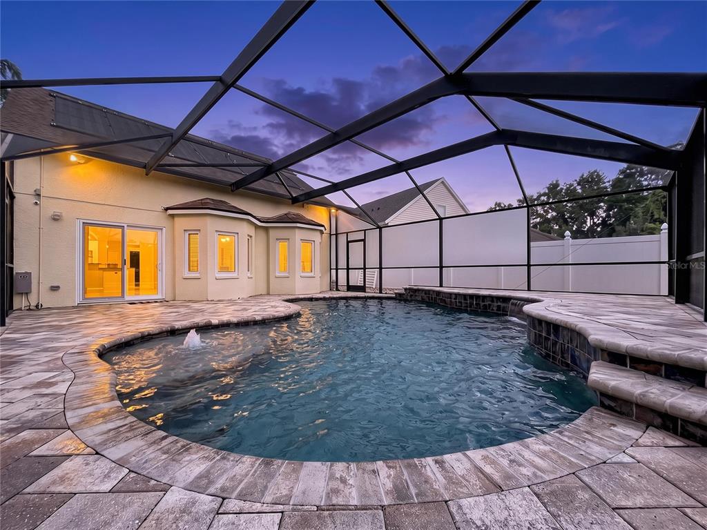 A swimming pool with a water feature inside a screened-in patio area at dusk — 5003 PRAIRIE VIEW WAY, WESLEY CHAPEL, FL