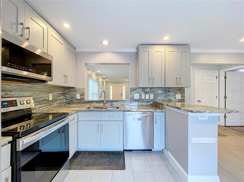 A kitchen features light gray cabinets, stainless steel appliances, and a stone-patterned backsplash and countertop — 5003 PRAIRIE VIEW WAY, WESLEY CHAPEL, FL