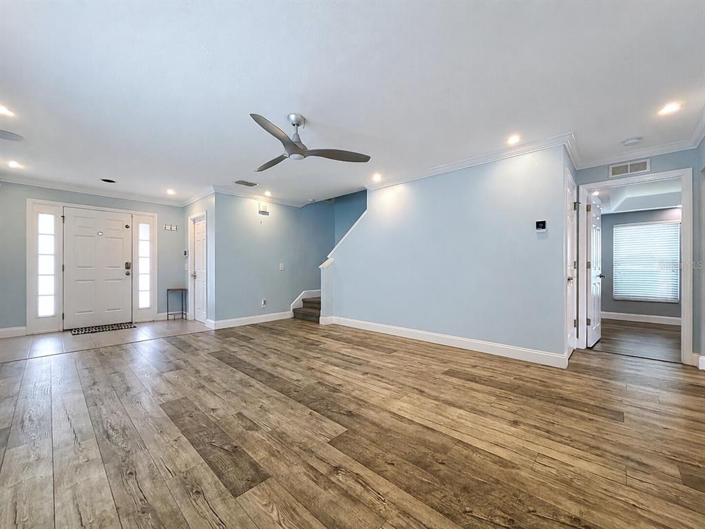 A spacious room with light blue walls, wood-look flooring, a ceiling fan, and a staircase — 5003 PRAIRIE VIEW WAY, WESLEY CHAPEL, FL