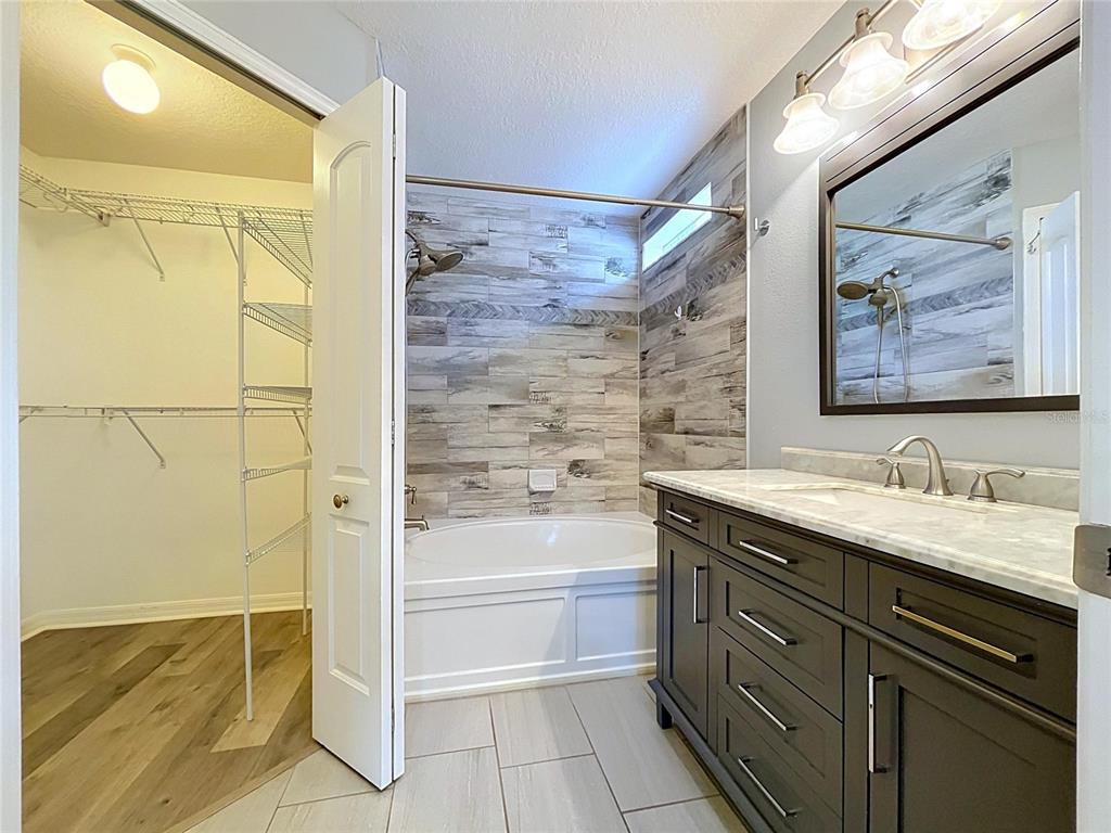 A bathroom features a dark vanity, a soaking tub with wood-look tile, and an adjacent closet — 5003 PRAIRIE VIEW WAY, WESLEY CHAPEL, FL
