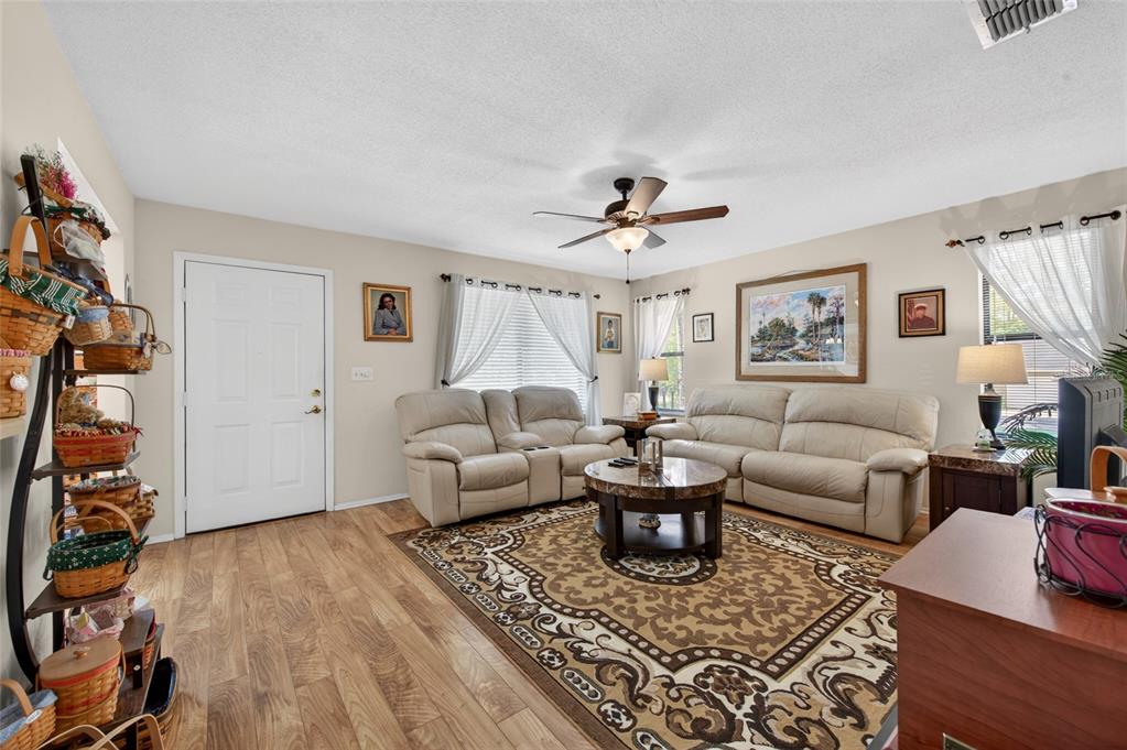 A living room features light-colored sofas, a patterned area rug, and wood-look flooring — 10 LAKEPOINT CIRCLE, PORT ORANGE, FL
