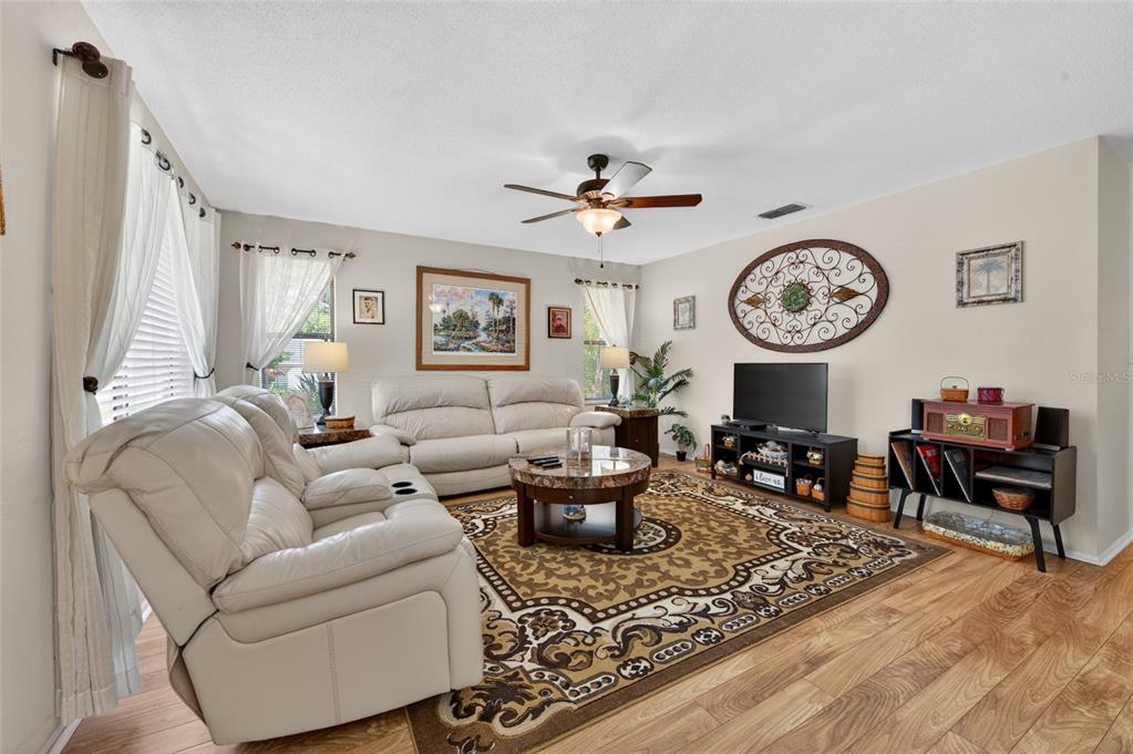 A living room features light-colored leather sofas, a patterned area rug, and wood-look flooring — 10 LAKEPOINT CIRCLE, PORT ORANGE, FL