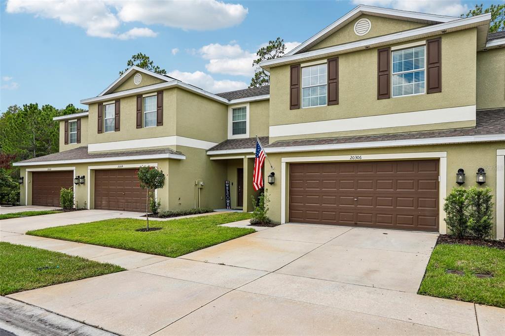 A two-story townhouse exterior with tan stucco walls, brown garage doors, and a small lawn — 20306 STARFINDER WAY, TAMPA, FL