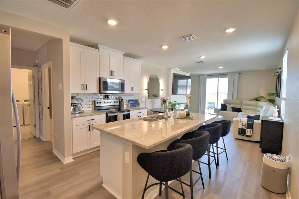 A kitchen with white cabinets and a granite island overlooks a living area with seating — 3563 BROADWING BOULEVARD, KISSIMMEE, FL