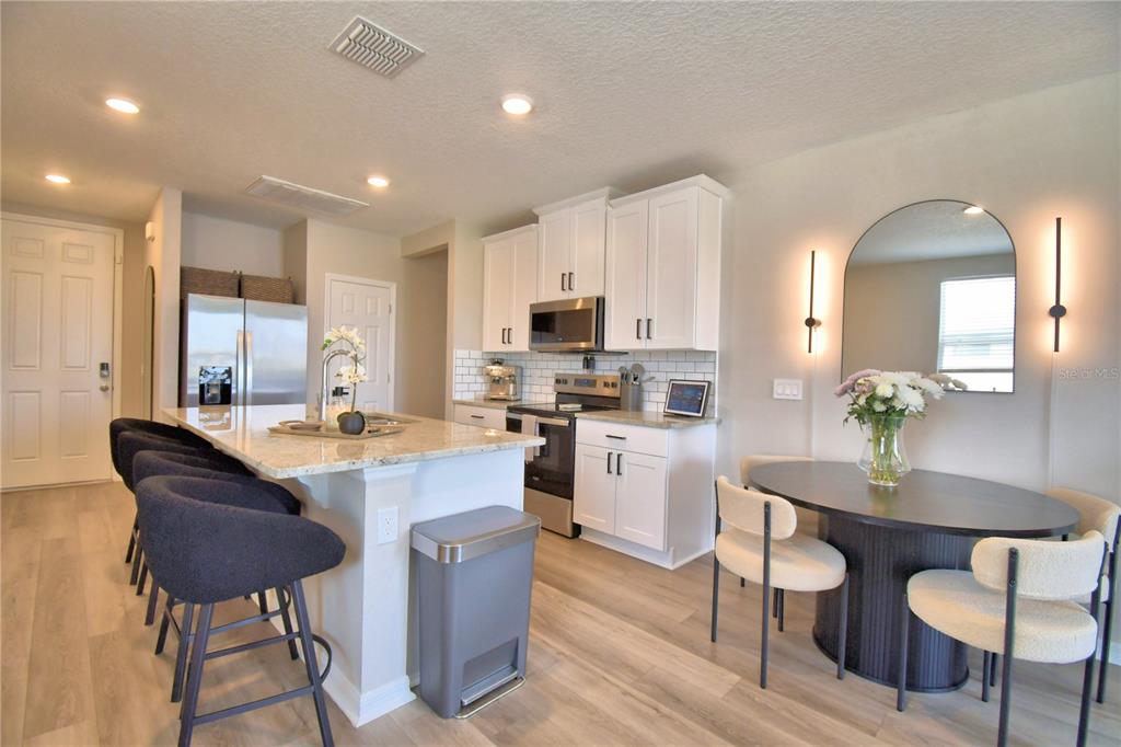 A kitchen features white cabinets, granite countertops, a center island, and an adjacent dining area — 3563 BROADWING BOULEVARD, KISSIMMEE, FL