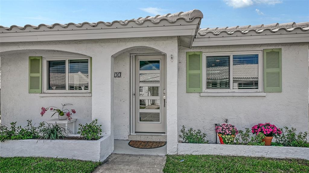 The exterior of a white stucco home features green shutters, a glass-paneled door, and planters — 900 SPANISH DRIVE N, LONGBOAT KEY, FL