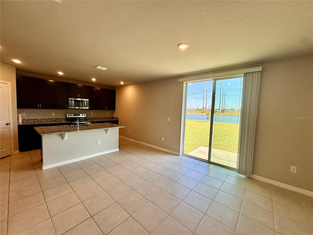 An open-concept kitchen with dark cabinets and granite countertops overlooks a living area with sliders — 10062 DAYBREAK GLEN, PARRISH, FL