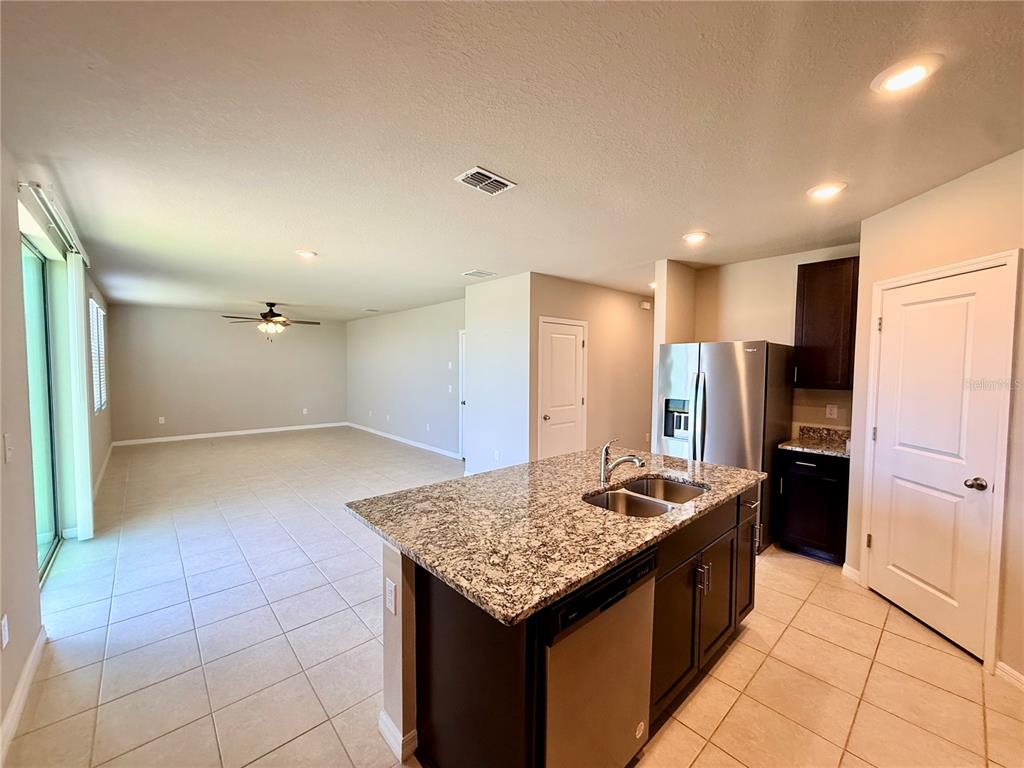 A kitchen island with granite countertops overlooks an open-concept living area with tile flooring — 10062 DAYBREAK GLEN, PARRISH, FL