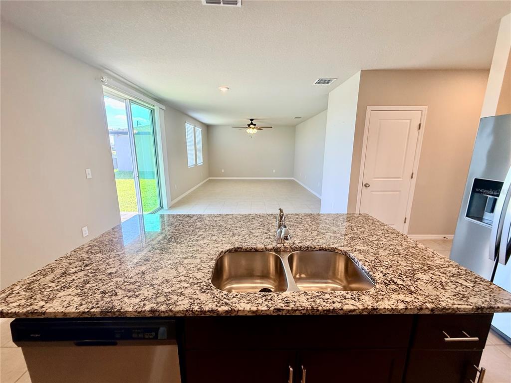A kitchen island with a double sink and granite countertop overlooks an open living area — 10062 DAYBREAK GLEN, PARRISH, FL