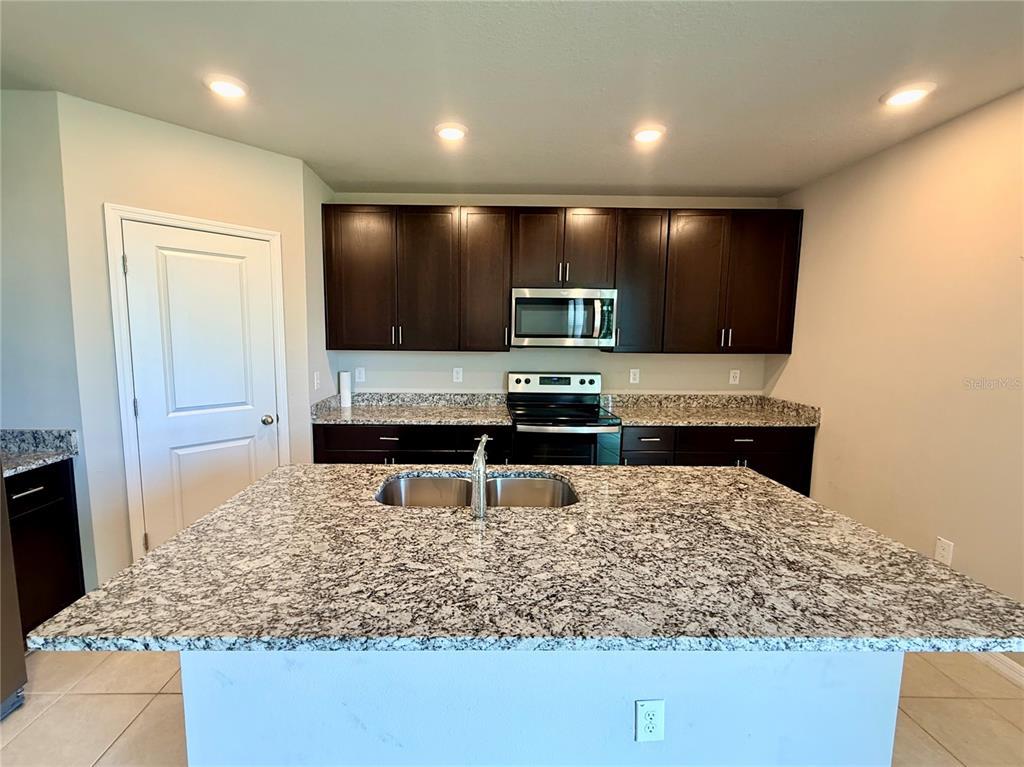 A kitchen features dark wood cabinets, granite countertops, a central island, and stainless steel appliances — 10062 DAYBREAK GLEN, PARRISH, FL