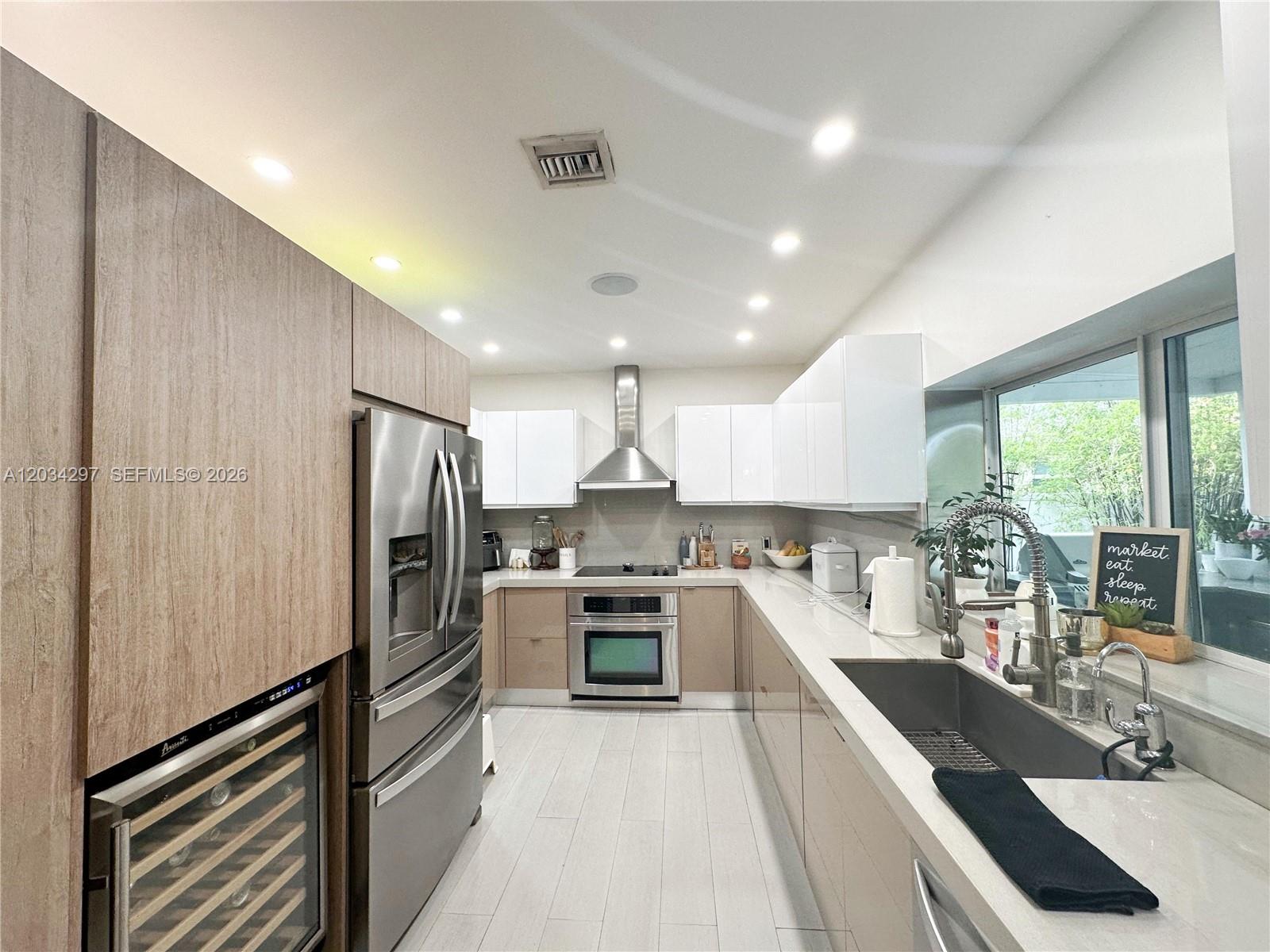 A modern kitchen features two-toned cabinetry, stainless steel appliances, and a large undermount sink — 20931 NE 24th Ave, Miami FL 33180, MIAMI, FL