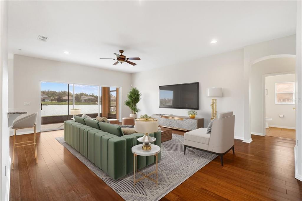 A living room features a green sofa, a television, and sliding doors overlooking a lake — 3533 SOMERSET CIRCLE, KISSIMMEE, FL