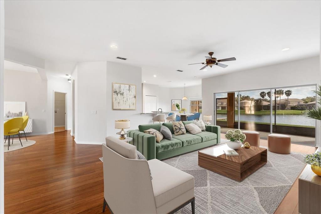 A living room with a green sofa, wood floors, and sliding doors overlooking a lake — 3533 SOMERSET CIRCLE, KISSIMMEE, FL