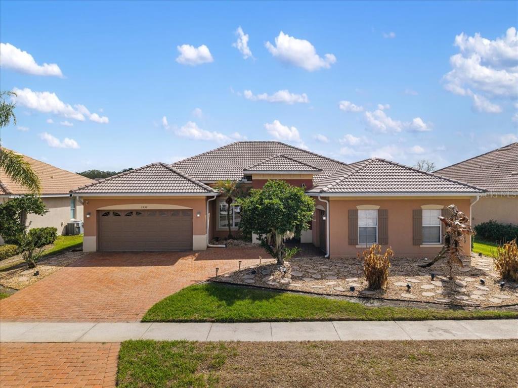 A single-story house with a tan stucco exterior, a tiled roof, and a brick driveway — 3533 SOMERSET CIRCLE, KISSIMMEE, FL
