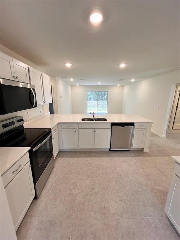 A kitchen features white cabinets, stainless steel appliances, and light-colored tile flooring — 10150 ISAACSON AVENUE, HASTINGS, FL