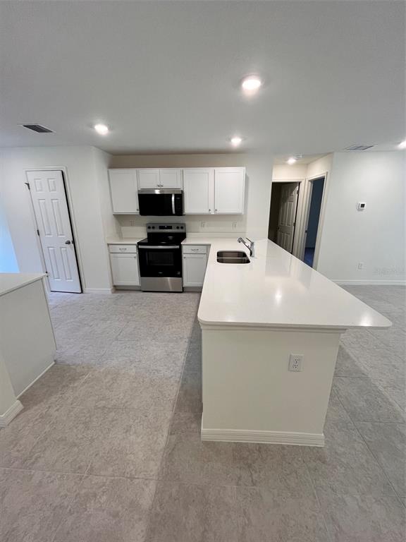 A kitchen features white cabinets, stainless steel appliances, and a large white quartz island — 10150 ISAACSON AVENUE, HASTINGS, FL