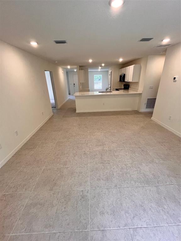 A spacious room with light-colored tile flooring leads to an open kitchen with white cabinets — 10150 ISAACSON AVENUE, HASTINGS, FL