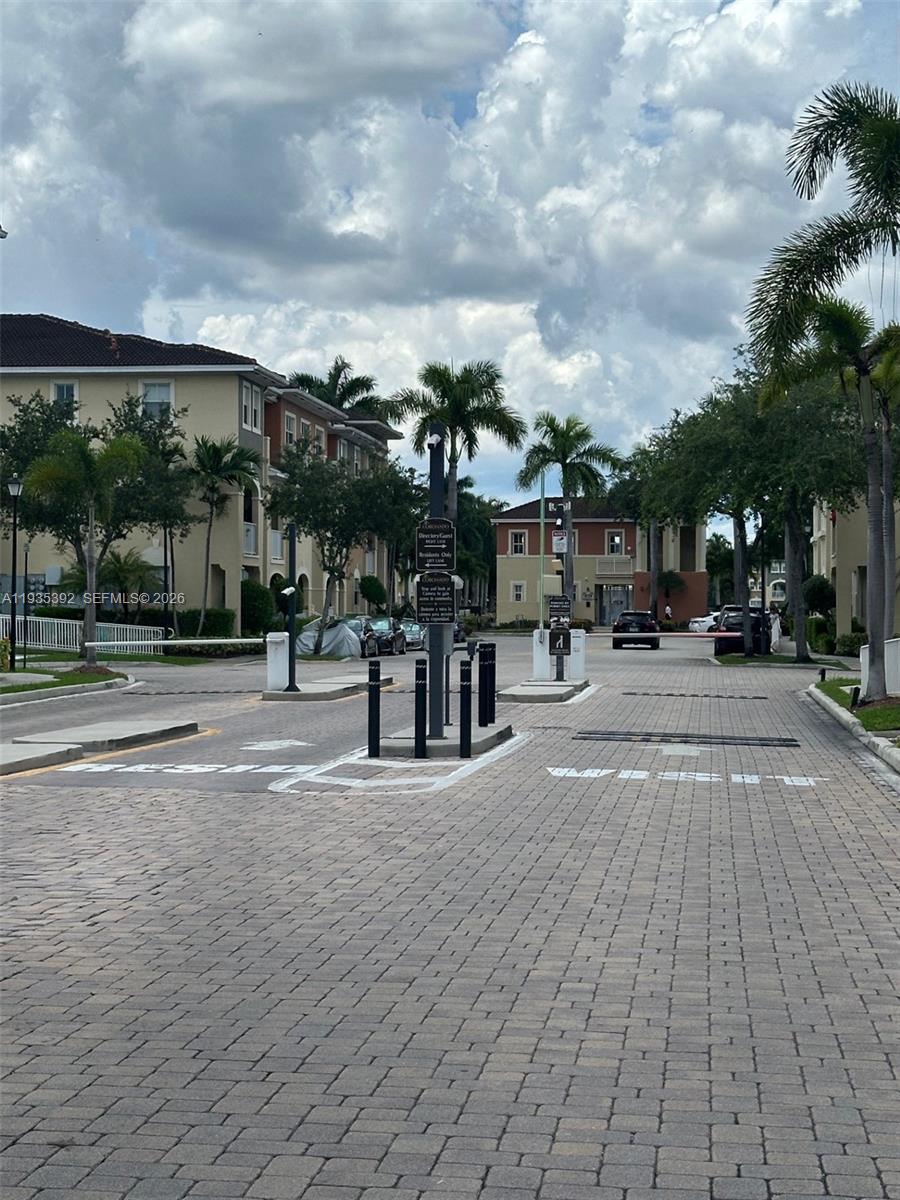 A gated entrance with a paved driveway leads to multi-story apartment buildings and palm trees — 10800 NW 88th Ter # 213, Doral FL 33178, DORAL, FL